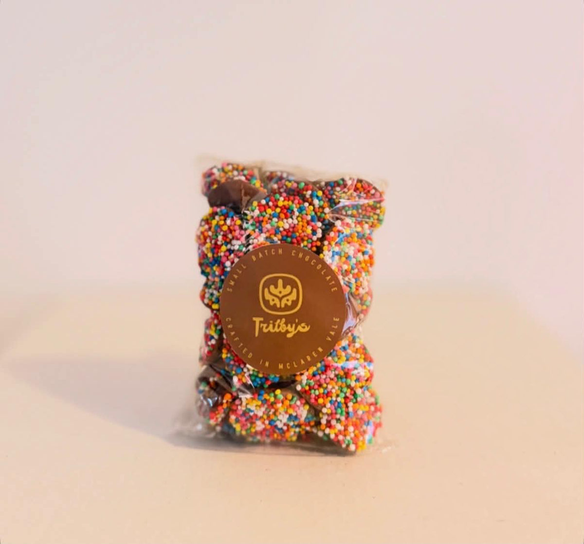 Milk chocolate speckles covered in rainbow sprinkles, in a clear bag with a Trilby's label